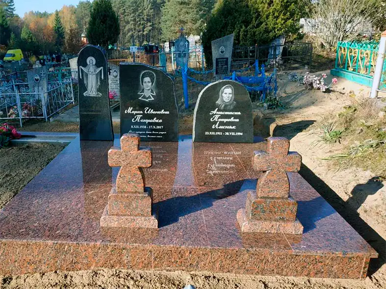 Двойной семейный памятник: две чёрные стелы с портретами и образом, перед ними два небольших креста из красного гранита на общей гранитной площадке