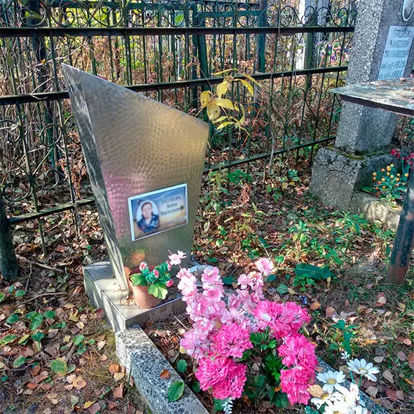 Памятник из оцинкованного металла с фотографией в ограде, перед ним цветы