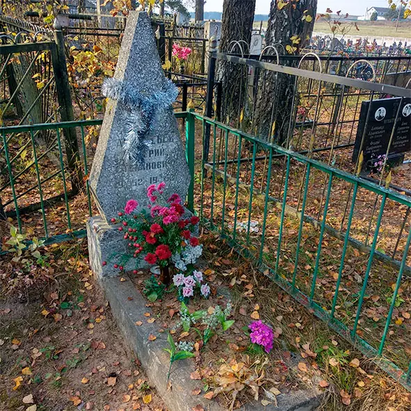 Бетонный памятник в форме вытянутого треугольного луча в зелёной ограде